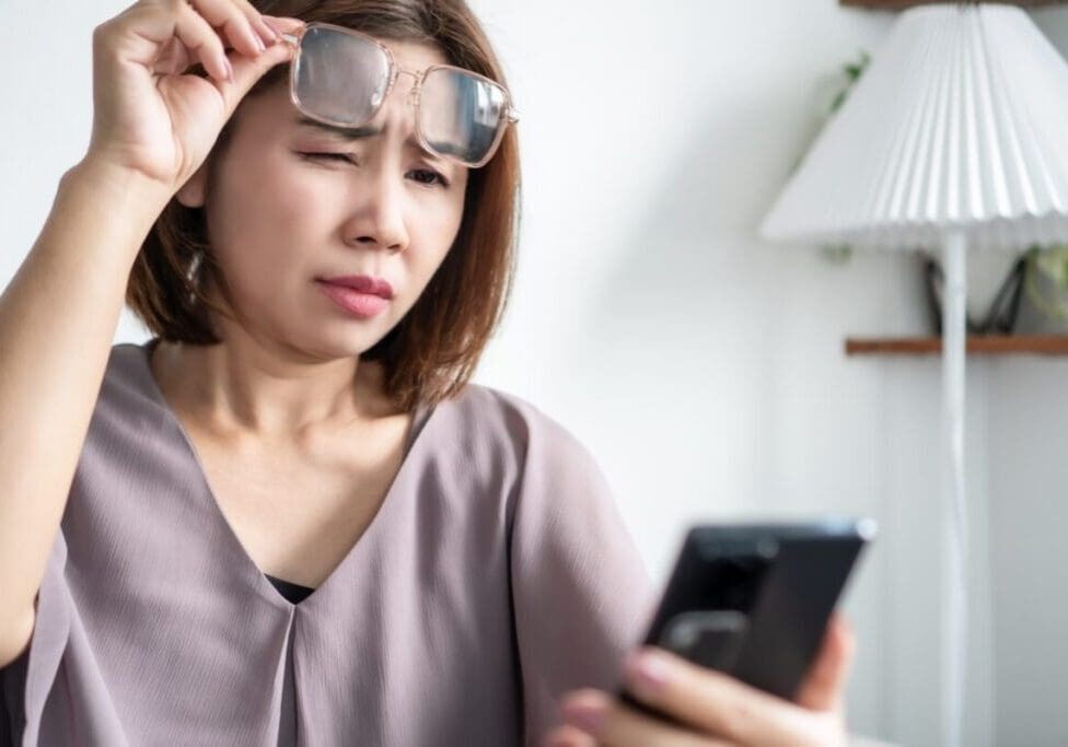 Woman squinting at smartphone while lifting glasses